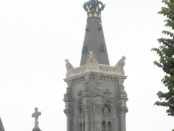 Stone tower spire with gargoyles and decorative stonework against an overcast sky