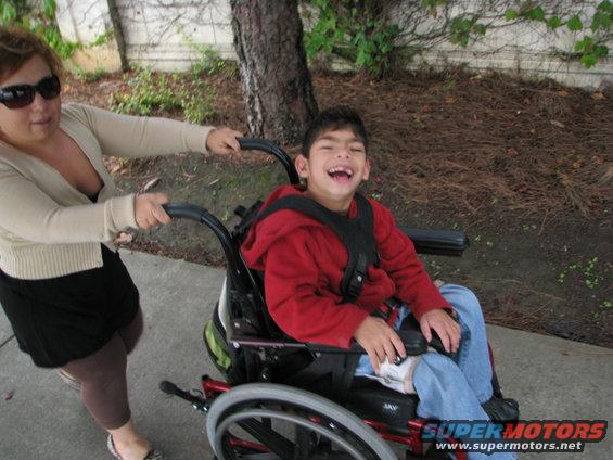 Child in red hoodie and jeans in wheelchair, pushed by woman in cardigan and black skirt