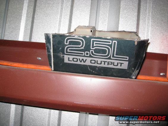 Close-up of a dark green badge that says "2.5L LOW OUTPUT" in silver lettering
