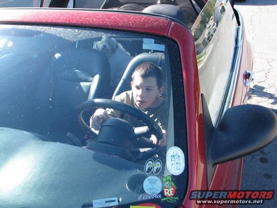 Interior view of a red convertible with a boy driving and a dog in the back