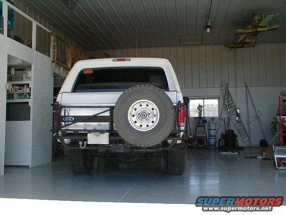 White Ford Bronco with a rear-mounted spare tire and aftermarket bumper parked in a garage
