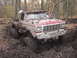 1990 Ford Bronco - This heavily modified Ford pickup truck is deeply embedded in thick mud and appears to be stuck in a wooded area.