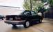 1989 Ford Escort - This black sedan is parked on a wet surface next to a building.