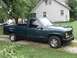 1995 GMC Sierra 1500 - A dark green 1995 GMC Sierra 1500 pickup truck is parked on a gravel driveway in front of a house.