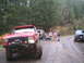 1989 Ford Bronco - A group of people and dogs stand on a dirt road next to a lifted red SUV with off-road modifications.