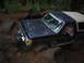 1989 Ford Bronco - A black Ford Bronco with a tan top is shown off-roading through mud and rocks, with a driver visible.
