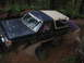 1989 Ford Bronco - A dark blue Ford Bronco with a tan top is stuck in mud on a wooded trail, with a person pushing from behind.