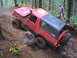 1989 Ford Bronco - This red Ford Bronco navigates a challenging off-road trail, demonstrating its capabilities on rough terrain.