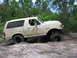 1989 Ford Bronco - This lifted 1989 Ford Bronco navigates a muddy trail with large off-road tires.