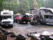 1979 Ford Bronco - A campsite scene with multiple vehicles including a red SUV and two RVs parked in a wooded area.