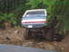1979 Ford Bronco - 1979 Ford Bronco navigating a challenging muddy off-road path surrounded by dense forest.
