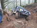 1979 Ford Bronco - A modified black SUV navigates a challenging muddy off-road course in a forest.
