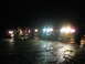 1979 Ford Bronco - Several trucks are parked on a wet road at night, illuminated by their headlights, with a group of people gathered nearby.