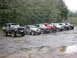 1979 Ford Bronco - A line of off-road vehicles, including a 1979 Ford Bronco, parked on a muddy lot.