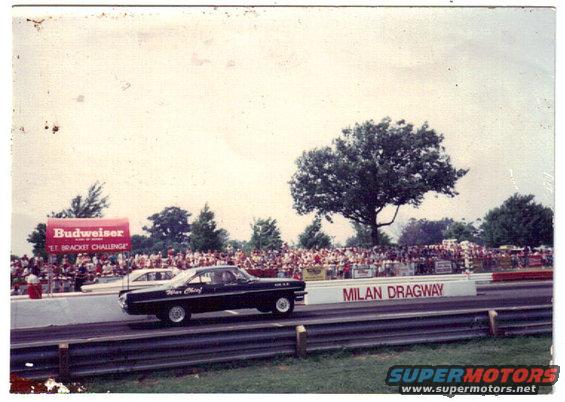 Black 1963 Ford Galaxie sedan racing on a drag strip, side view, with "Milan Dragway" signage