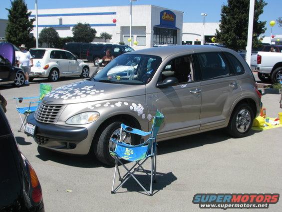 Tan 2005 Chrysler PT Cruiser with white flower decals on hood and fender, parked outside with chairs