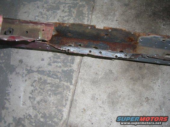 Rusted red metal frame with numerous holes, resting on a concrete floor