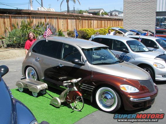 Two-tone brown and tan Chrysler PT Cruiser with whitewall tires and American flags on the roof