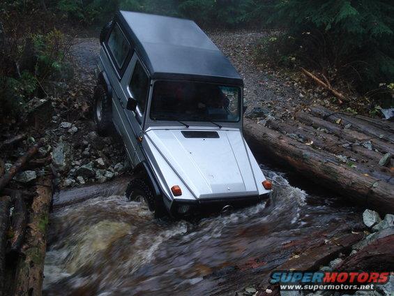 Silver Mercedes-Benz G-Wagen crossing a stream on a log bridge