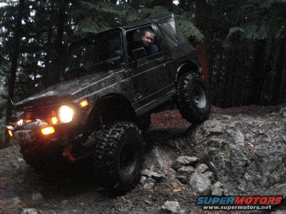 Black off-road vehicle with soft top driving over rocks in a forest