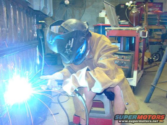 Welder wearing a helmet and leather apron, sparks flying from a welding torch in a workshop
