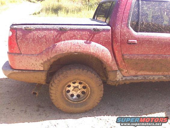 Mud-covered red 2001 Ford Explorer pickup truck, side view showing rear wheel and bed cover