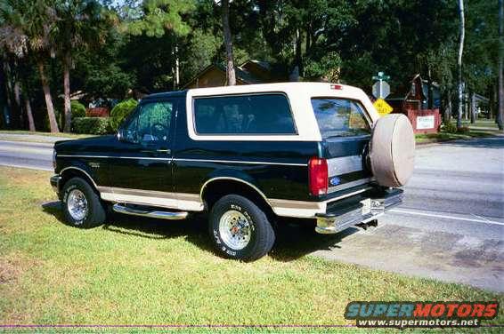 1992 Ford Bronco parked on grass next to a road, with a spare tire mounted on the rear