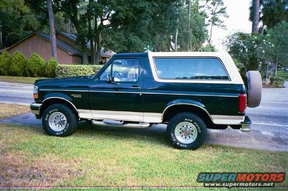Side view of a dark green 1992 Ford Bronco with a white top and spare tire on the back