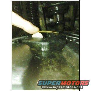 Finger pointing at a white plastic cap on a black engine component with yellow residue