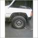 1985 Ford Bronco - A white SUV sits with its hood open, revealing the engine bay and front wheel assembly.