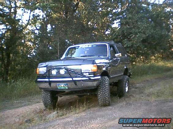 Dark gray Ford Bronco with aftermarket grille guard and off-road tires parked on a dirt road