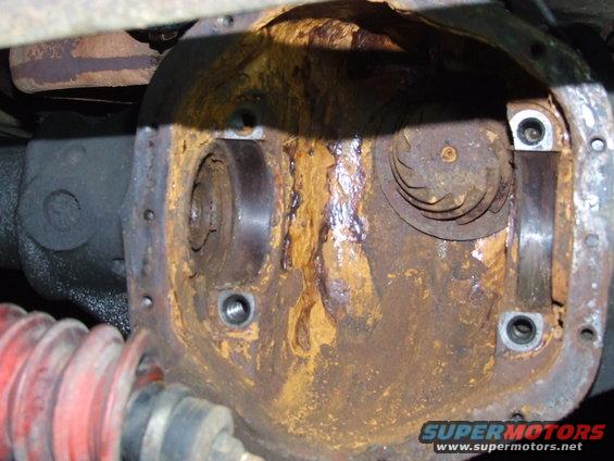 Close-up of a rusty differential cover with internal gears visible. A red boot is on the left