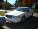 2001 Ford Crown Victoria - A white 2001 Ford Crown Victoria is parked on a driveway under a tree with autumn leaves.