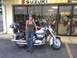 2006 Suzuki VL 1500 Intruder Classic - A woman poses with a motorcycle in front of a Suzuki dealership, with other bikes visible inside.