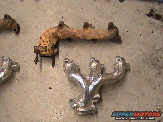 two exhaust manifolds on concrete floor, one rusty, one shiny