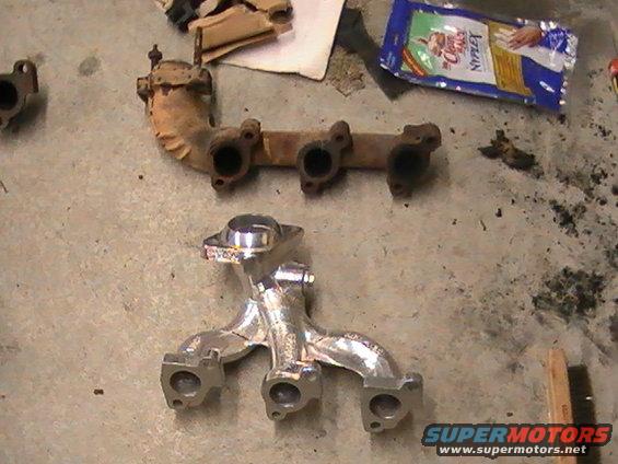 Two exhaust manifolds on a concrete floor; one is rusty and old, the other is shiny and new