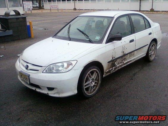 White Honda Civic sedan with mud splattered on the side, parked on wet asphalt