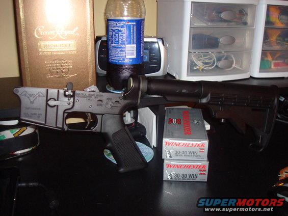 AR-15 lower receiver with engraved bat logo, two boxes of Winchester 30-30 WIN ammunition, and a bottle of soda