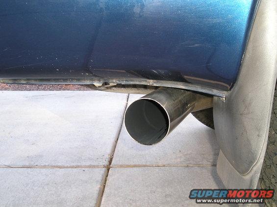 Close-up of a shiny exhaust pipe exiting the rear of a blue vehicle, with a mud flap visible
