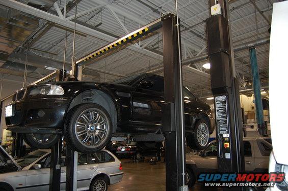 2002 BMW M3 on a lift in a garage, another car below