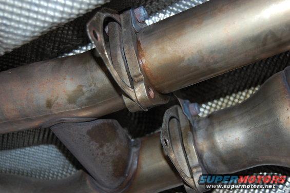Close-up of exhaust pipes and catalytic converter flanges under a vehicle