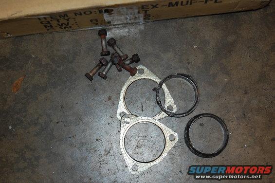Exhaust gaskets and bolts on a concrete floor. Box in background has text