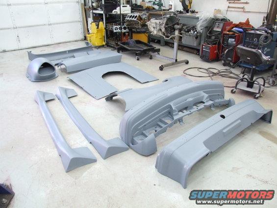 Gray car body parts laid out on a workshop floor, including bumpers and fender flares