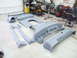 1990 Ford Mustang - Various unpainted car body panels are arranged on the floor of a garage, with an engine and tools in the background.