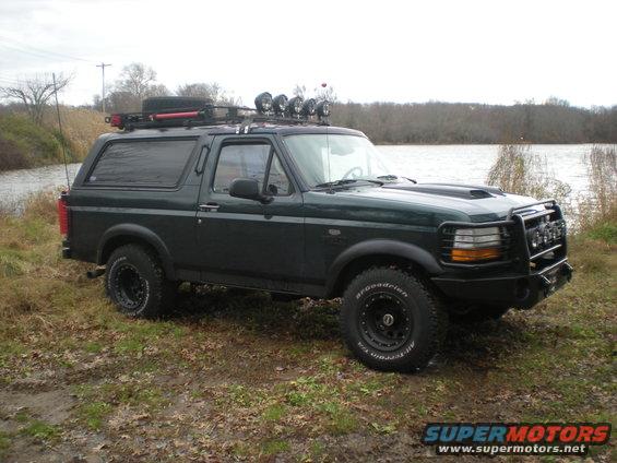 1993 Ford Bronco with roof rack and off-road lights parked by a lake