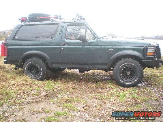 Green 1993 Ford Bronco side view with roof rack and spare tire