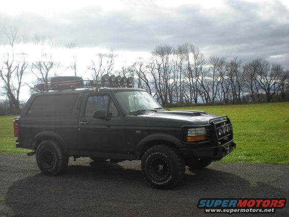 Dark green Ford Bronco with roof rack and off-road lights parked on a gravel road