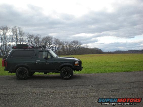 Dark green 1993 Ford Bronco parked on a gravel road with a grassy field behind it