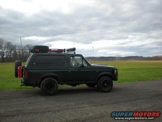 Dark green 1993 Ford Bronco side view with roof rack and spare tire
