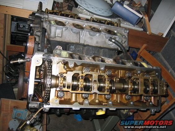 Engine block with camshafts and timing chain exposed. Some parts are disassembled